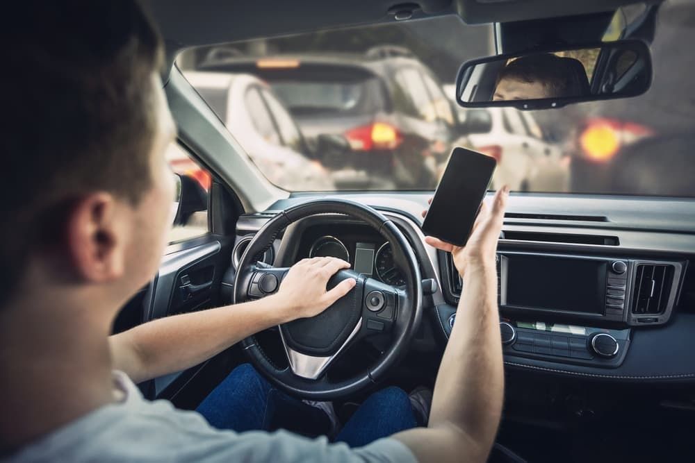 Driver holding a smartphone while steering a car in traffic.