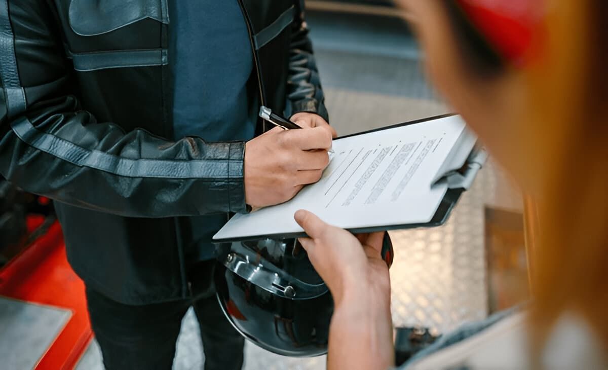 Biker signs insurance papers to collect repaired motorcycle.