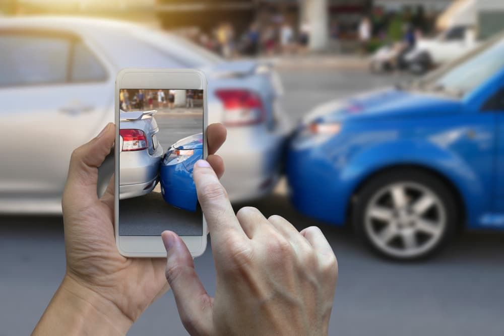 Driver using a smartphone to photograph damage after a rear-end car accident for evidence