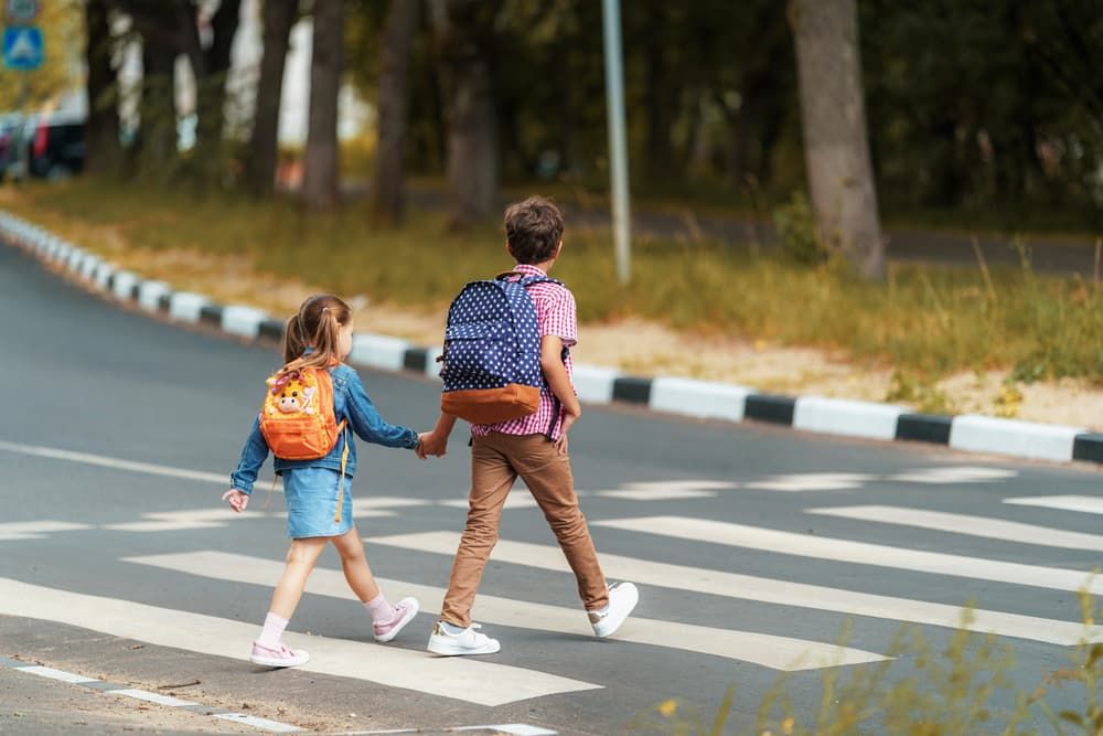 A boy and girl wearing backpacks cautiously use the crosswalk while heading to school.