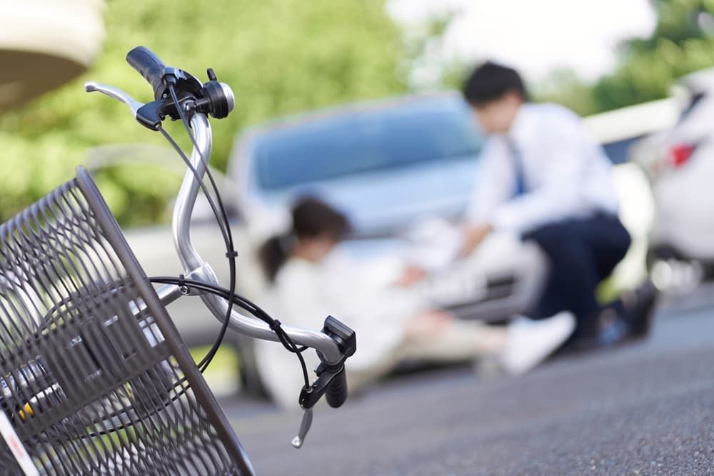 A fallen bicycle in focus, with a blurred accident scene involving a cyclist and car.