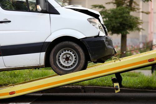 Damaged white van being loaded onto a tow truck after an accident.