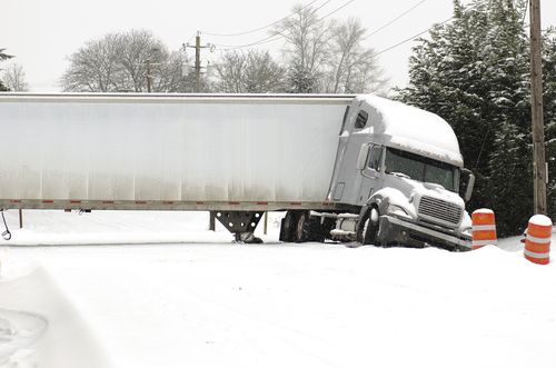 Jackknifed semi truck blocking a snowy road after losing control with the trailer folded at an angle.