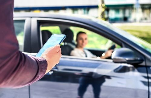 Man using a smartphone to request a ride while a rideshare driver waits in a car.