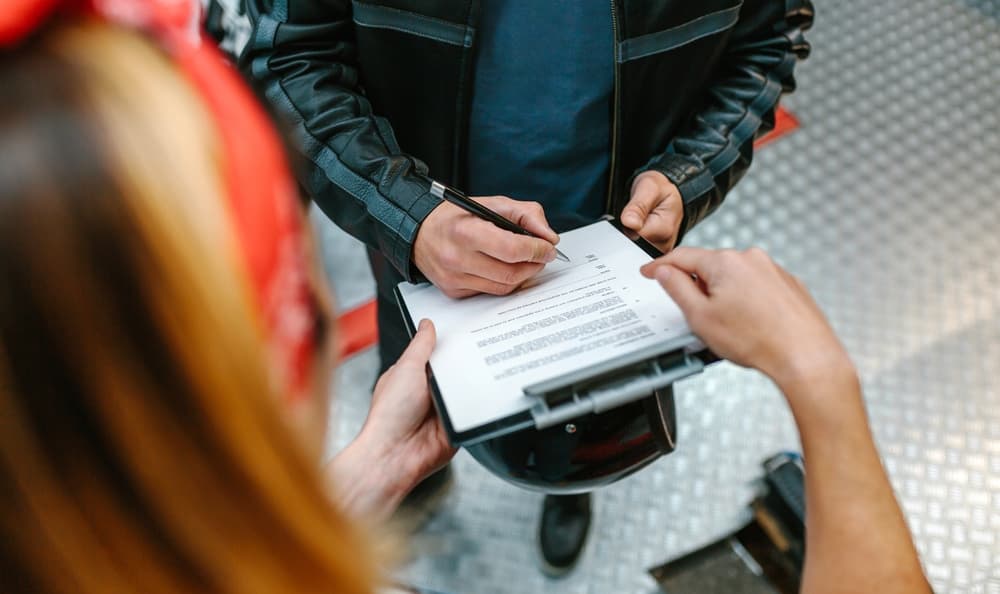 Motorcyclist signs claim form for compensation after distracted driver accident.