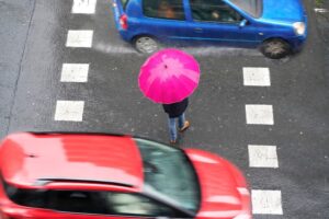 Pedestrians in crosswalk face danger from fast-moving city traffic, highlighting risks of unsafe driving behavior.