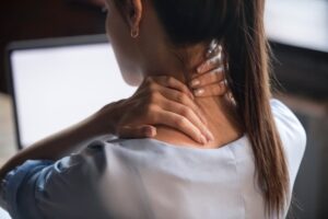 Woman rubbing sore neck and shoulders, experiencing whiplash pain from a recent accident-related neck injury.