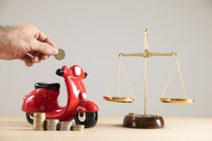 Red motorbike piggy bank beside scales and coins, symbolizing financial battles with insurance companies after accidents.