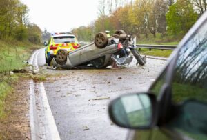 Car lying upside down after a crash on a motorway with a police car beside it.
