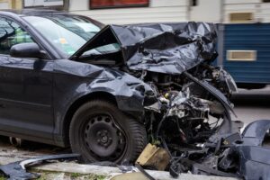 Severely damaged black car after a crash, showing why insurers may lowball your totaled car’s value.
