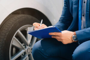 Insurance adjuster taking notes beside a damaged car