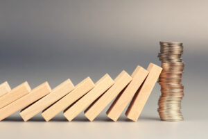 Wooden domino blocks falling toward a stack of coins representing financial protection or stability.
