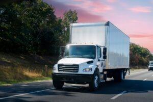 White box delivery truck driving on a highway during sunset.