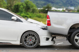 White sedan with front end damage after rear ending a gray pickup truck on a city street