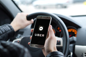 Person holding a smartphone with the Uber app open while driving a car.