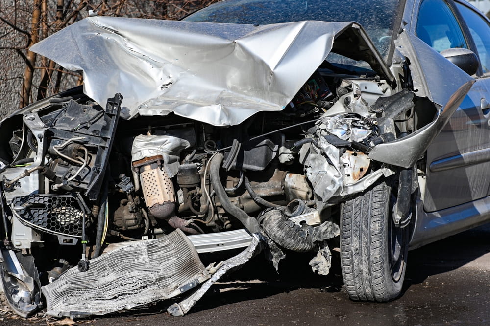 Silver car with severe front-end damage exposing the engine