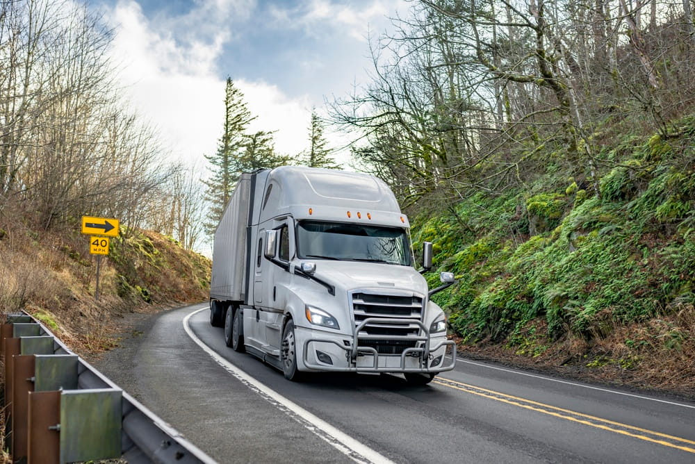Semi-truck navigating a curved road with a reduced speed limit sign