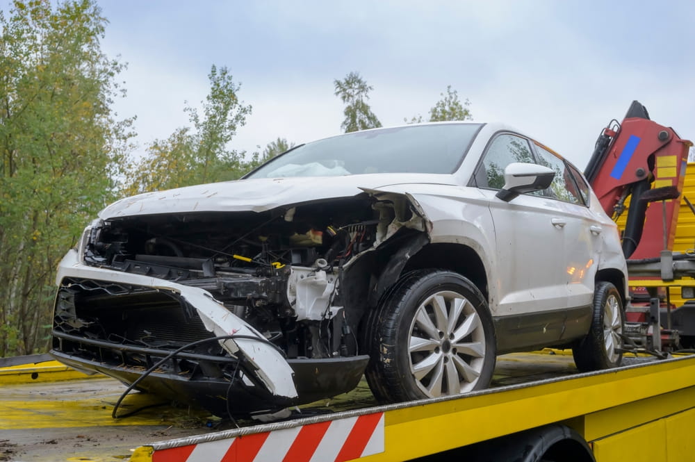 Wrecked white SUV loaded onto a tow truck flatbed